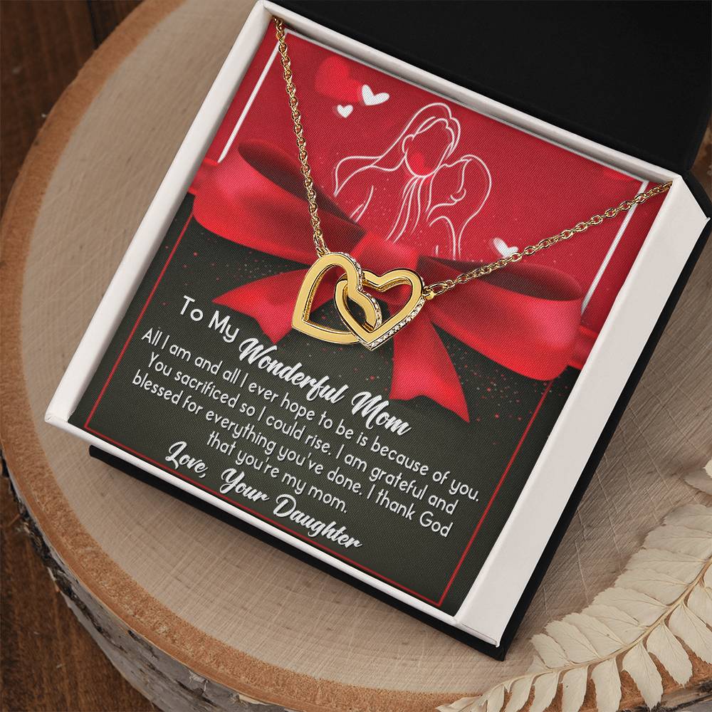 The "To Mom, Because Of You - Interlocking Hearts Necklace" in rose gold with cubic zirconia rests in an open box, accompanied by a heartfelt message card from a daughter to her mom.