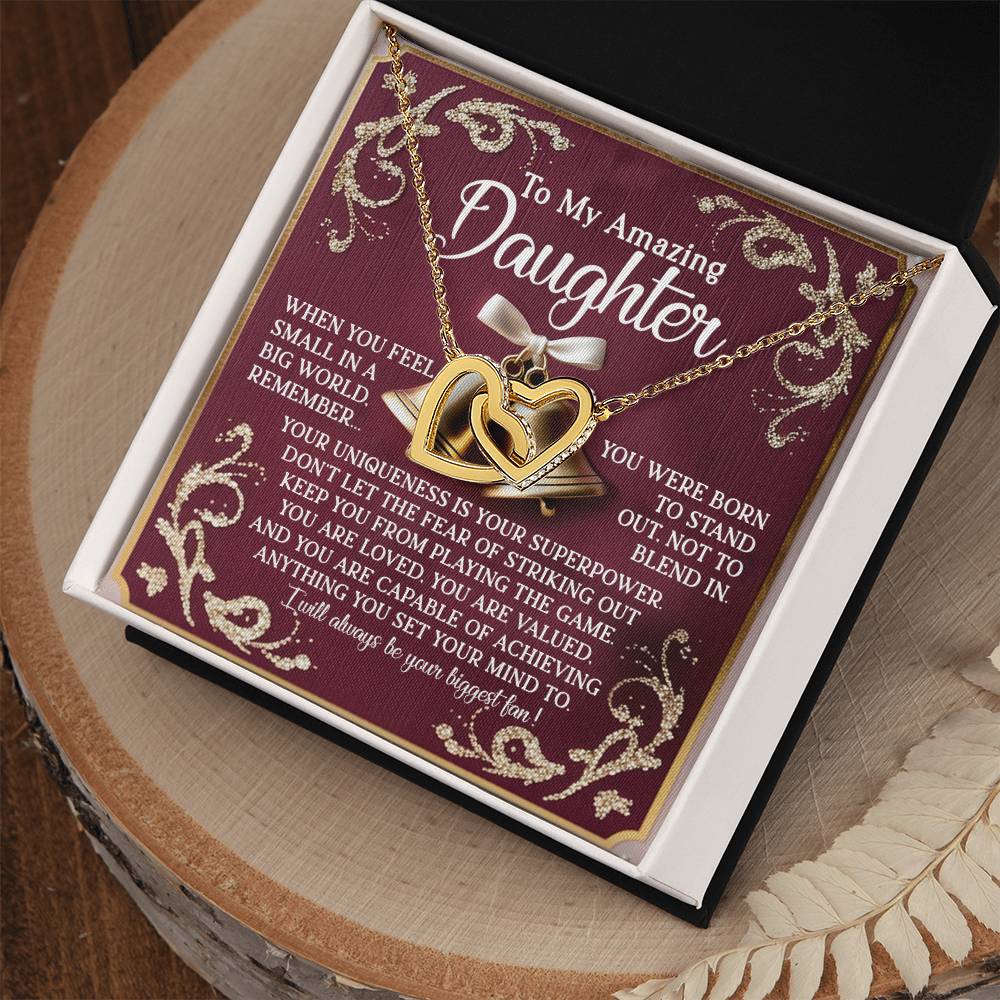 The Daughter-Stand Out - Interlocking Hearts Necklace features a gold heart with a rose-gold finish and a smaller intertwined heart. It comes in an elegant box with a heartfelt message for your daughter, featuring floral designs and decorative borders on a burgundy background.