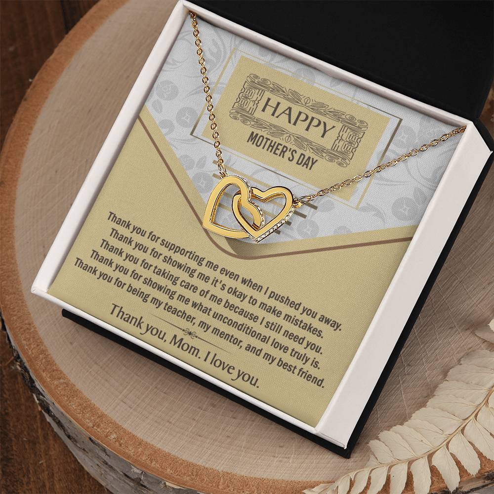 The Mother's Day-Thank You - Interlocking Hearts Necklace, adorned with cubic zirconia crystals, comes in a gift box with a "Happy Mother's Day" card expressing love and gratitude. Dried leaves add a charming accent beside the box.