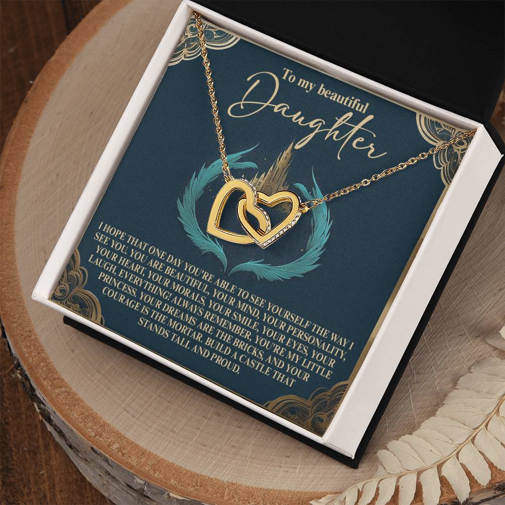 The Daughter-Little Princess Interlocking Hearts Necklace features a rose gold finish and cubic zirconia crystals. It comes in an elegant box with a heartfelt message card for your daughter, all beautifully displayed on a wooden surface with feather accents.