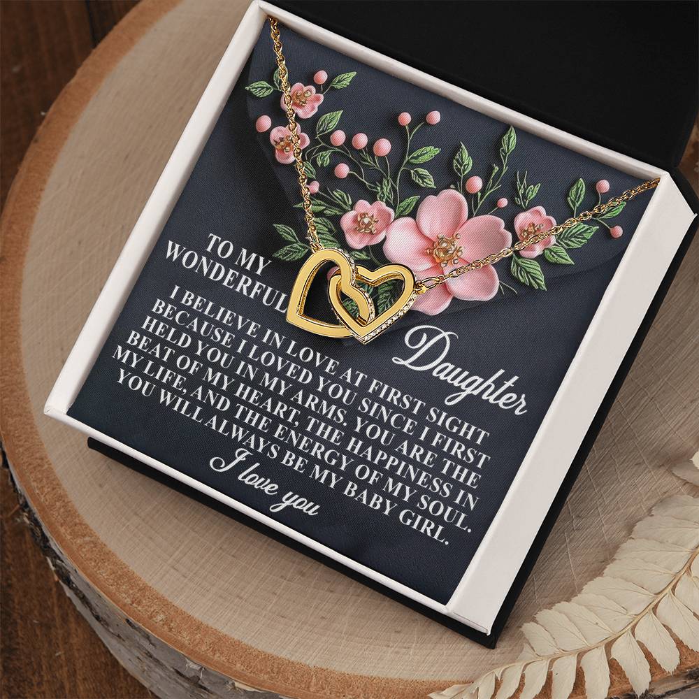 The Daughter-Love Sight necklace, featuring a gold interlocking hearts design with a rose gold finish and floral motifs, is beautifully showcased in a white box. The background includes pink flowers, green leaves, and a loving daughter-oriented message.