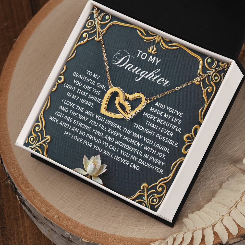 The Daughter-Never End Interlocking Hearts Necklace, with a rose gold finish, sparkles in a decorative box inscribed "To My Daughter," symbolizing love and admiration. The box is elegantly placed on a wooden surface featuring a lotus flower design.