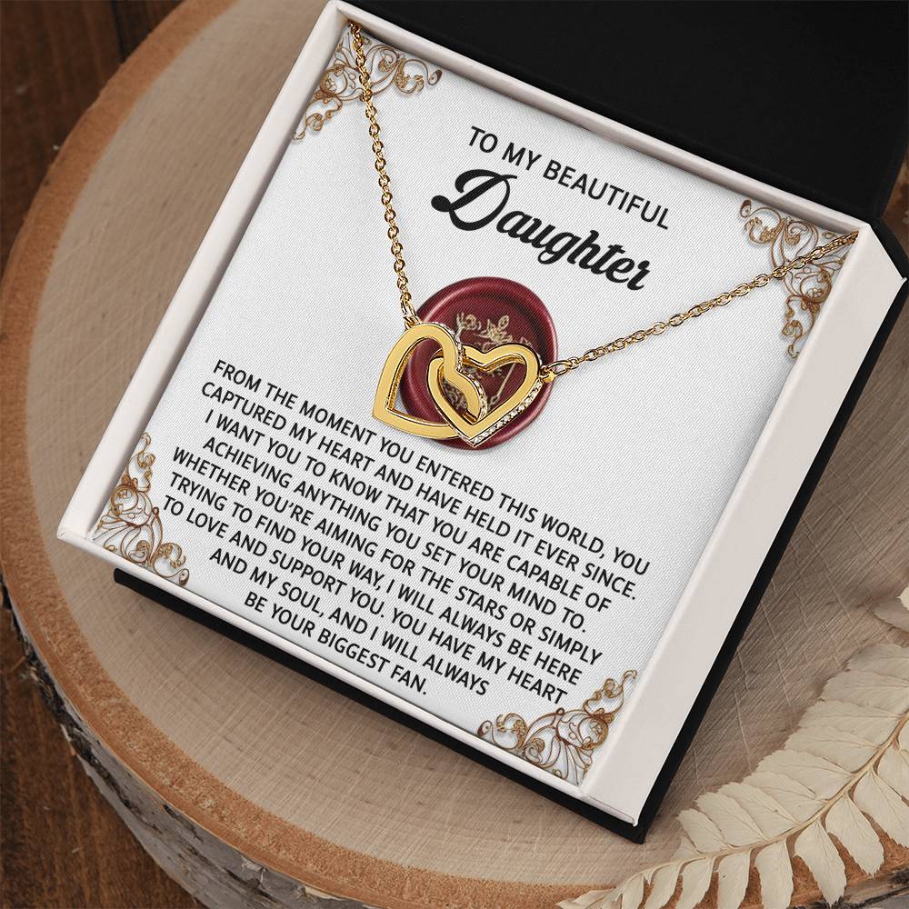 The Daughter-Biggest Fan Interlocking Hearts Necklace, with a rose gold finish, is presented in an open box. The card inside reads, "To my beautiful daughter," conveying a heartfelt message of love and support, accented with sparkling cubic zirconia crystals.