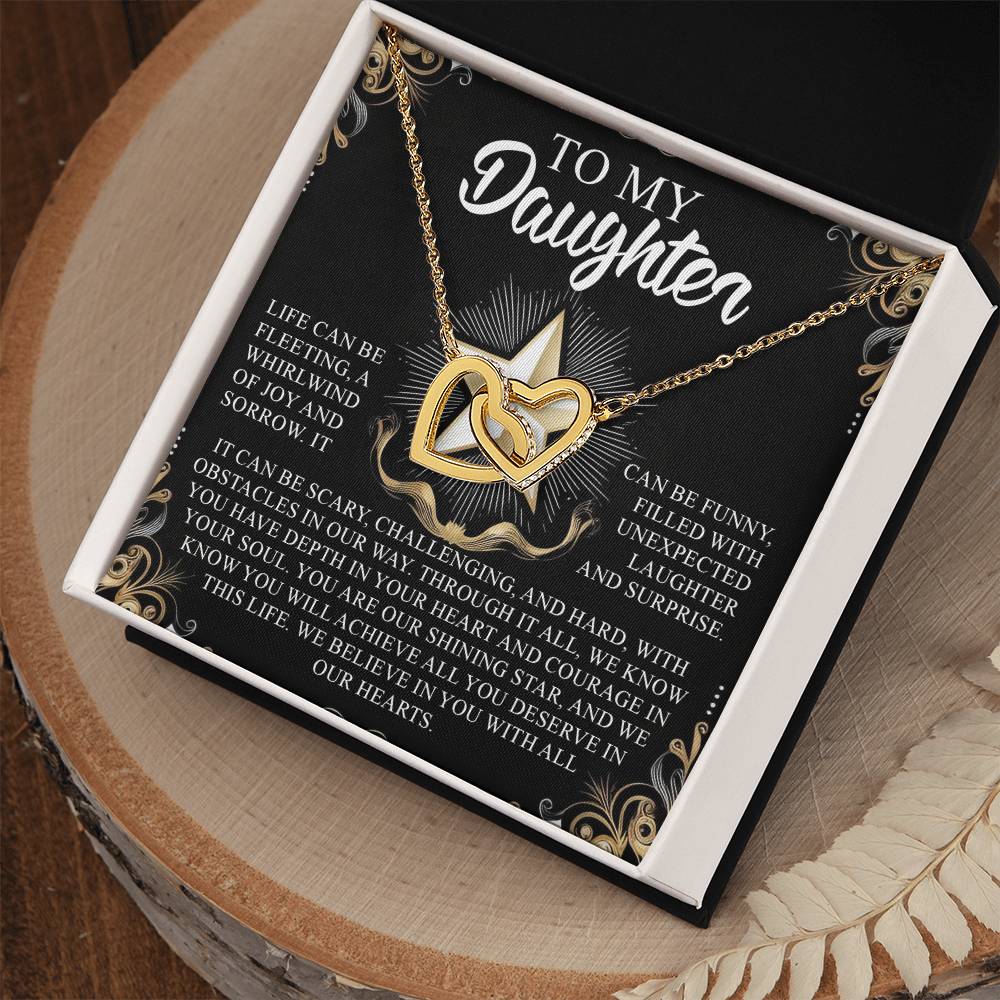 An open gift box on a decorative wooden surface reveals the Daughter-Shining Star Interlocking Hearts Necklace with rose gold finish and cubic zirconia crystals. The lid bears a heartfelt message to a daughter, expressing love, support, and encouragement.