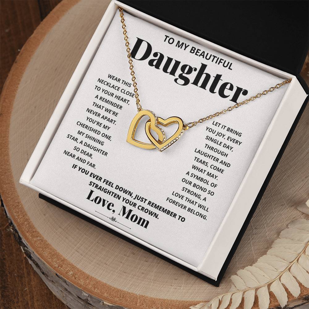 A "To My Beautiful Daughter, Wear This Necklace - Interlocking Hearts Necklace" with interlocking hearts pendants adorned with cubic zirconia crystals, presented in a box with a heartfelt message from a mother to her daughter.