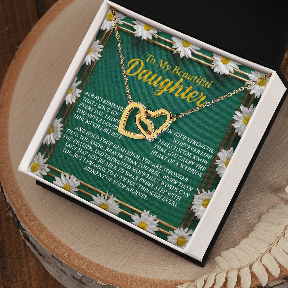 The Daughter-Your Journey - Interlocking Hearts Necklace, featuring a gold design with cubic zirconia crystals, is displayed in an open box. The background has white daisies and a heartfelt message expressing love and encouragement to a daughter.