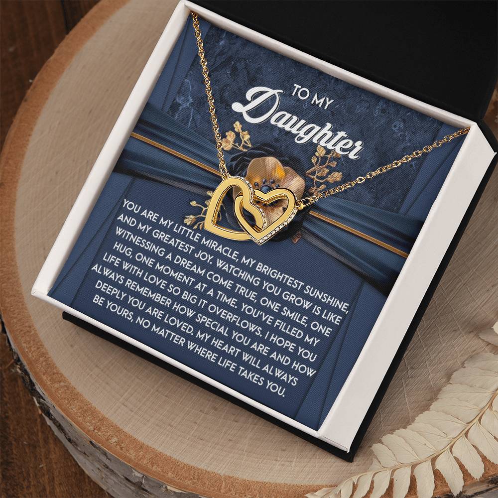 The Daughter-You Are Loved Interlocking Hearts Necklace, adorned with cubic zirconia and a rose gold finish, is set in a gift box. A note says "To My Daughter," conveying love. The box sits elegantly on wood.