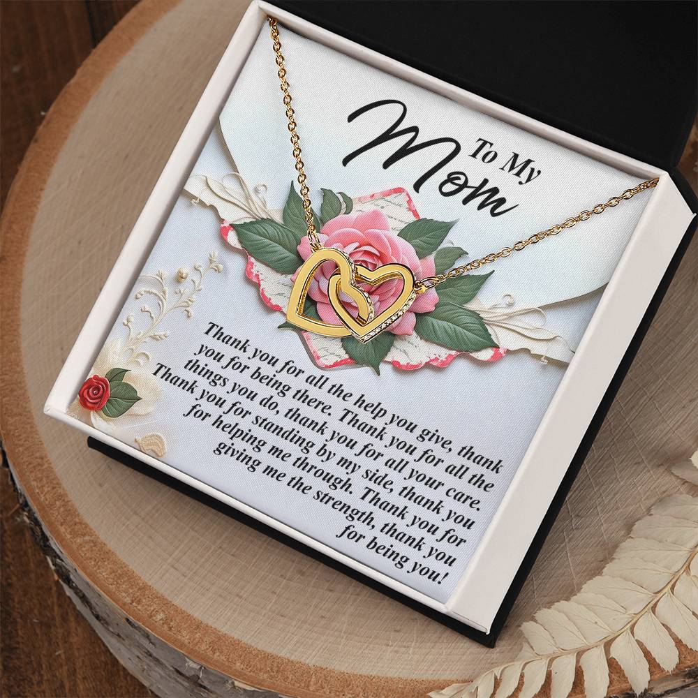 The Mom-Being You - Interlocking Hearts Necklace features a rose gold finish and sparkling cubic zirconia, presented in a gift box with a pink rose design. The heartfelt message expresses deep appreciation for a mother's support and care, making it an elegant gift resting on the wooden surface.