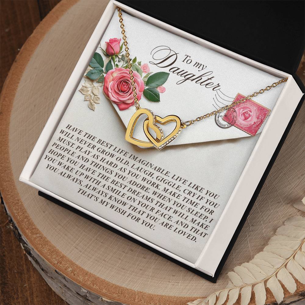 The Daughter-My Wish - Interlocking Hearts Necklace, with a rose gold finish, is displayed on a cushioned card reading "To my daughter" with a heartfelt message. The card features pink roses and a heart stamp, elegantly presented in an open black box on a wooden table.