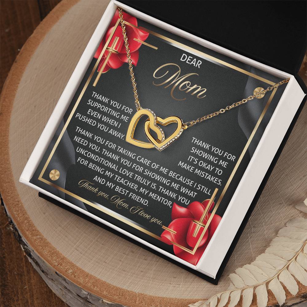 The Mom-Best Friend 2 - Interlocking Hearts Necklace in rose gold finish lies in an open black box. A heartfelt message for "Mom," surrounded by red roses and a thank you note, expresses love and gratitude, while cubic zirconia crystals add sparkle.