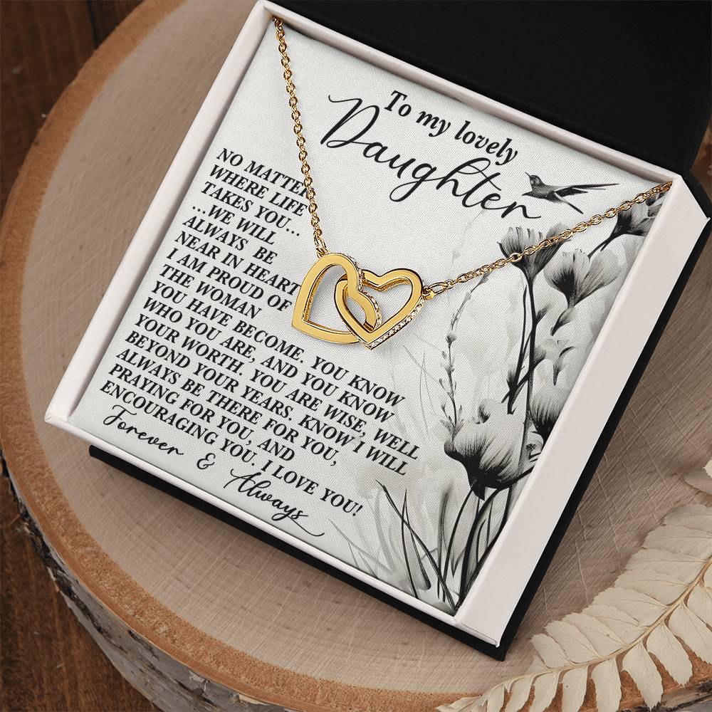 The Daughter-Heart Near Interlocking Hearts Necklace, crafted with surgical steel and a rose gold finish, rests on a card reading "To my lovely daughter." The card conveys love, support, and pride from parents and is embellished with a floral pattern, all beautifully presented in an open box.