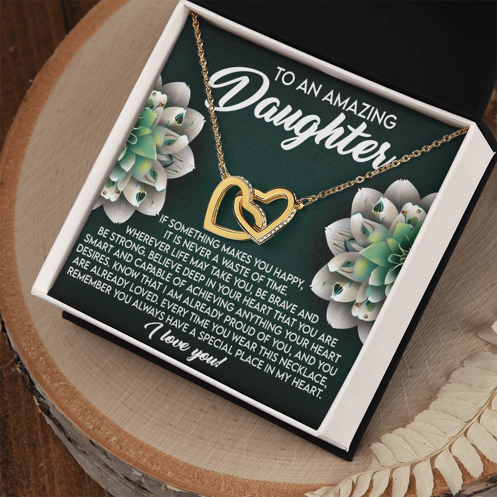 A gold Daughter-Special Place Interlocking Hearts Necklace with cubic zirconia is displayed in an open box. The lid reads "To an Amazing Daughter" with a heartfelt message, surrounded by white flowers on a green background, expressing love and encouragement.
