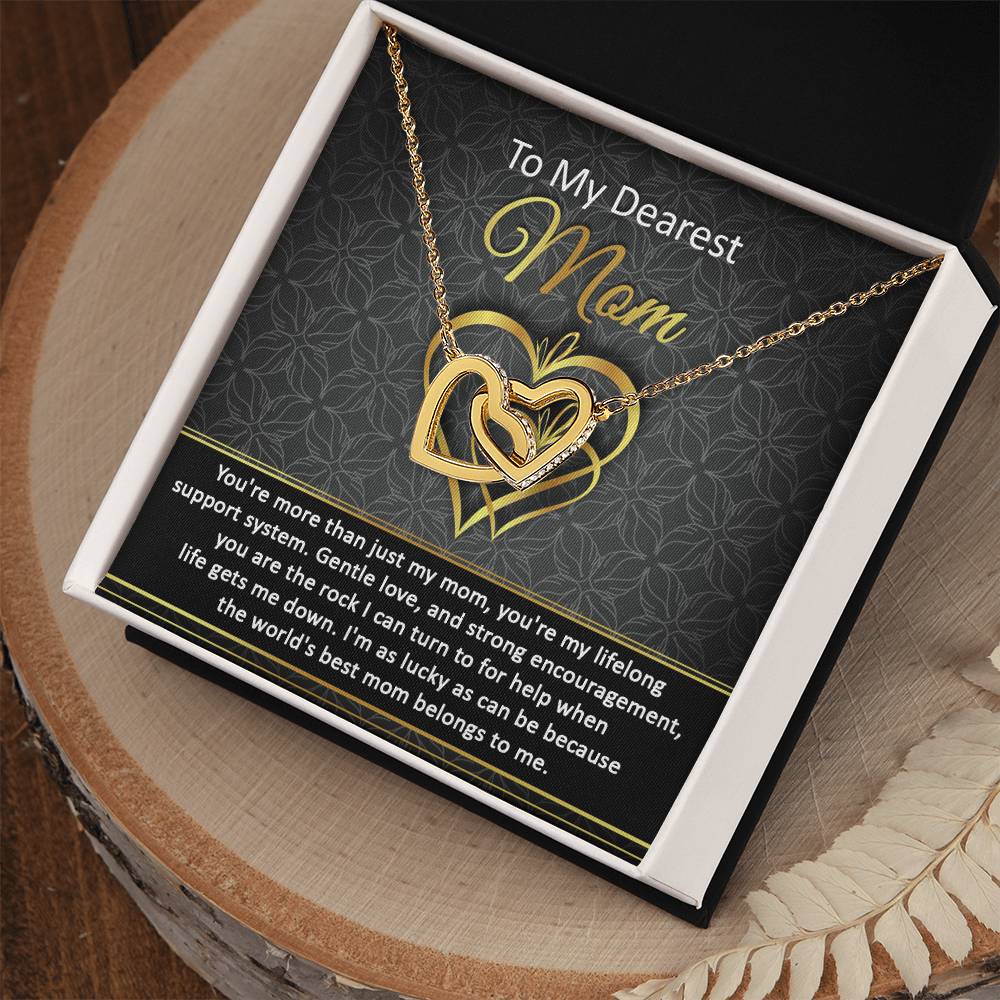 The "To Mom, Belongs To Me2" Interlocking Hearts Necklace is a gold heart necklace with "Mom" inscribed, adorned with cubic zirconia crystals in a gift box. It includes a heartfelt message of gratitude and love, embodying the essence of a personalized gift.