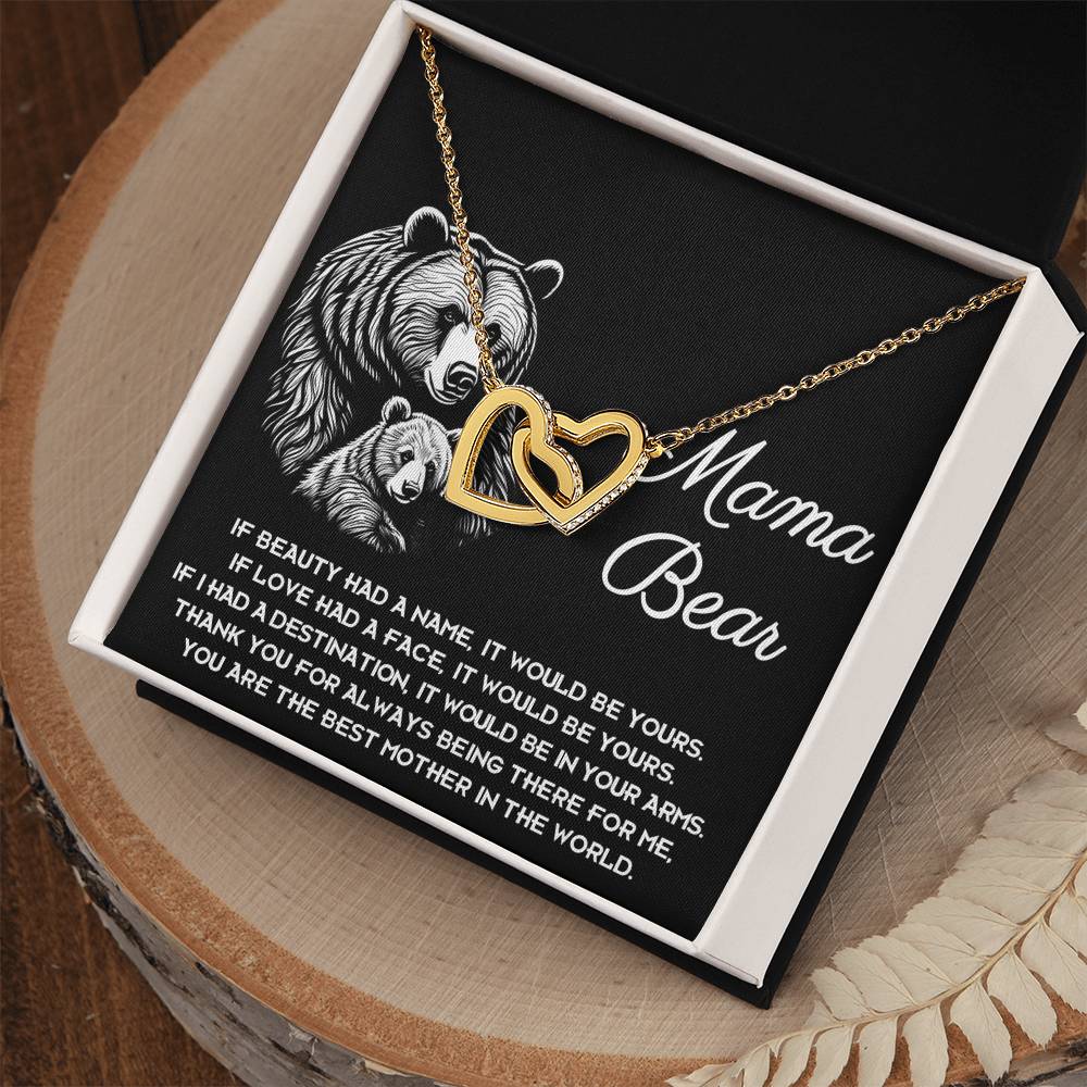 The "To Mom, In Your Arms - Interlocking Hearts Necklace," adorned with cubic zirconia crystals, is elegantly showcased in a box. Inside the lid, bear illustrations accompany the touching message "Mama Bear," making it an ideal personalized gift.