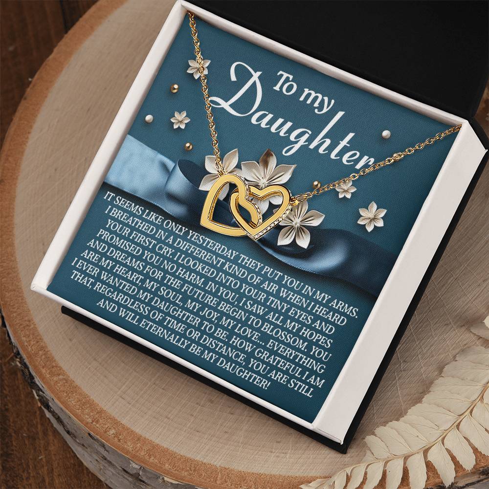 The Daughter-Hopes Dreams Interlocking Hearts Necklace in rose gold is showcased in a box labeled "To my Daughter," featuring a loving poem and decorative flowers on a teal background with cubic zirconia accents.