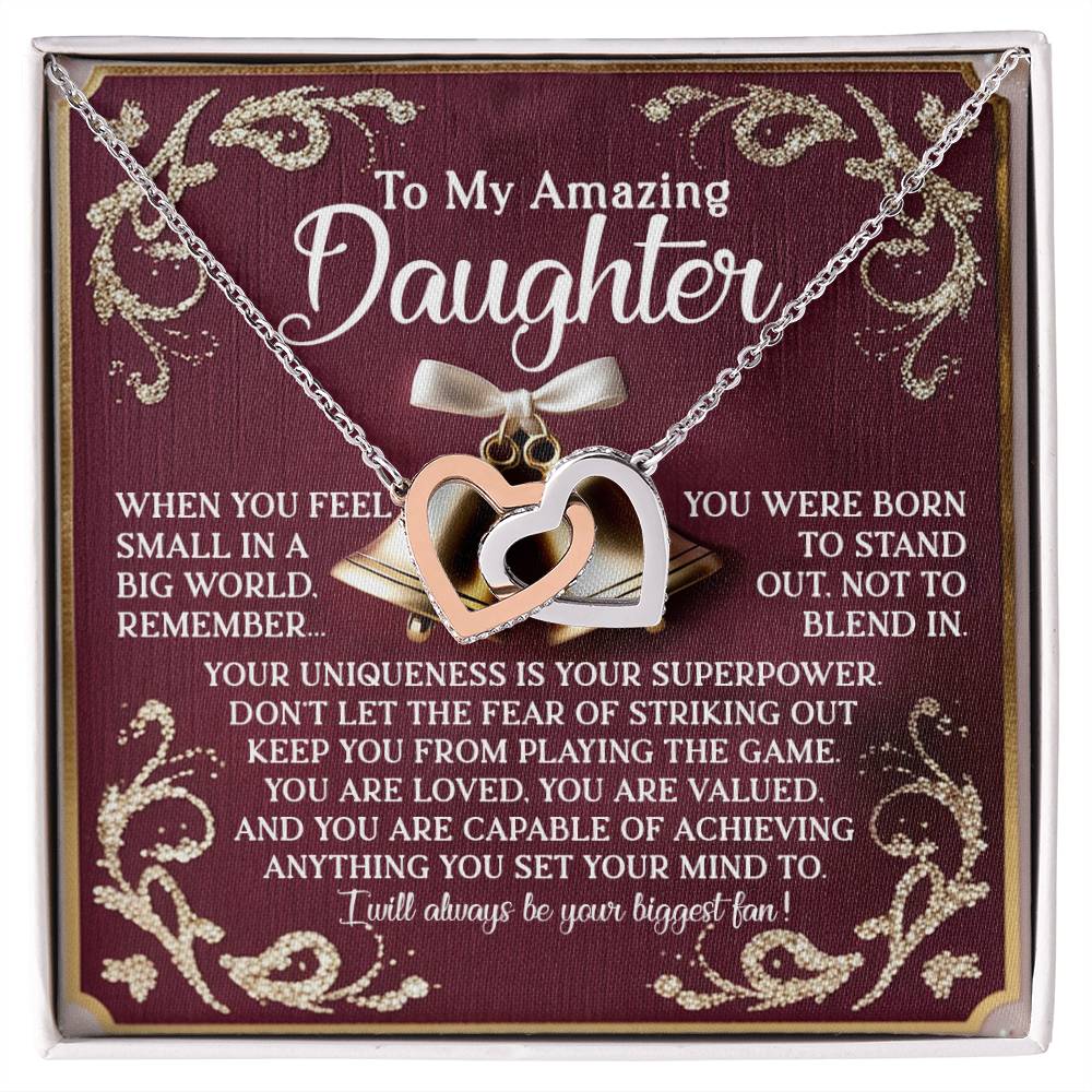 The Daughter-Stand Out Interlocking Hearts Necklace features a rose gold finish and a jewelry gift box with an inspirational message reading "To My Amazing Daughter" about uniqueness, value, and achieving goals. The burgundy background enhances the elegant gold details.