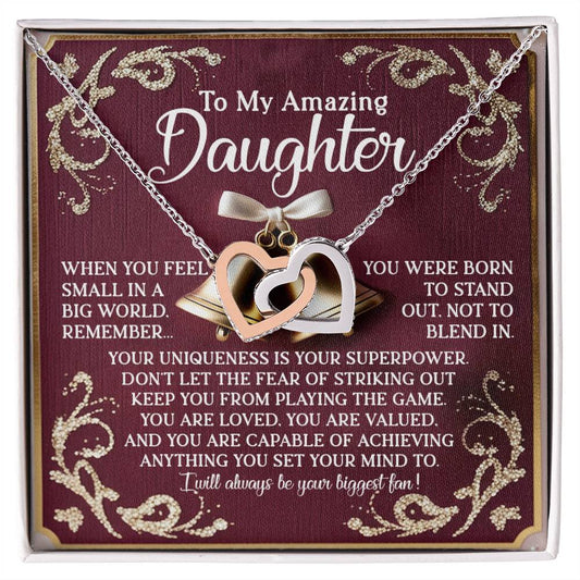 The Daughter-Stand Out Interlocking Hearts Necklace features a rose gold finish and a jewelry gift box with an inspirational message reading "To My Amazing Daughter" about uniqueness, value, and achieving goals. The burgundy background enhances the elegant gold details.