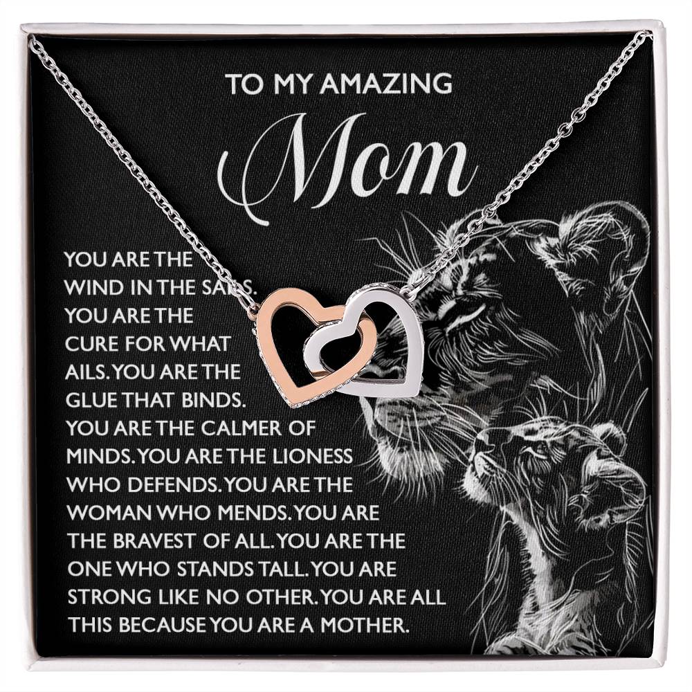 The "Mom-The Cure" Interlocking Hearts Necklace, crafted from surgical steel and rose gold, features intertwined hearts with cubic zirconia on a black background, a lion with its cub, and a touching message of gratitude for Mom's strength and love.