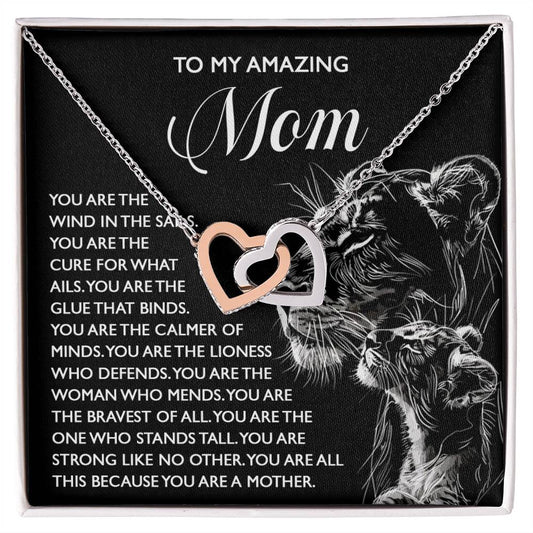 The "Mom-The Cure" Interlocking Hearts Necklace, crafted from surgical steel and rose gold, features intertwined hearts with cubic zirconia on a black background, a lion with its cub, and a touching message of gratitude for Mom's strength and love.