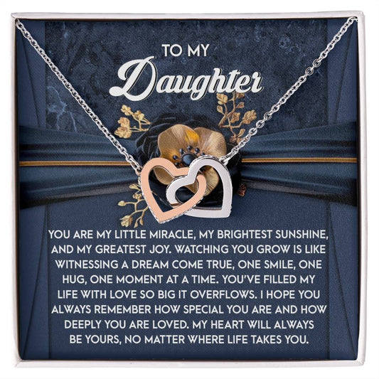 The "Daughter-You Are Loved - Interlocking Hearts Necklace," adorned with shimmering cubic zirconia, comes on a card stating "To my daughter" with a heartfelt message about love and joy, set against a floral design backdrop.