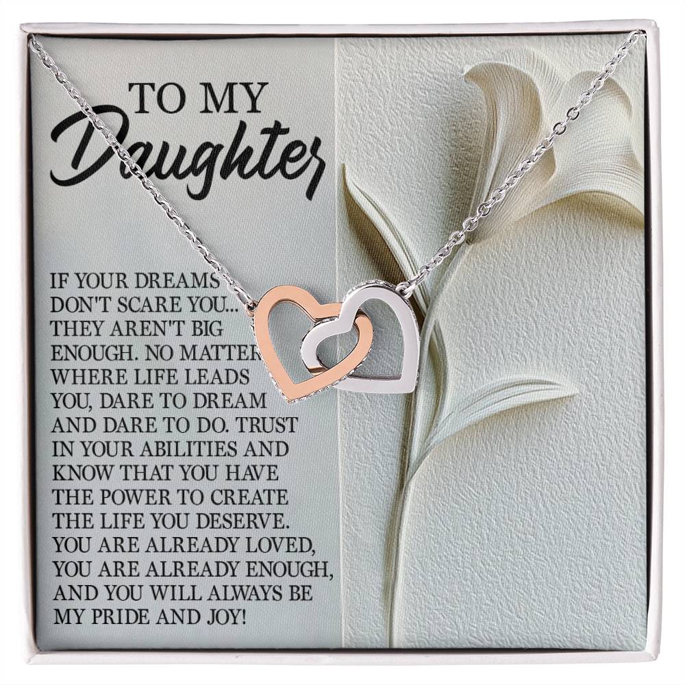 The Daughter-Dare Dream Interlocking Hearts Necklace in silver and rose gold with cubic zirconia crystals is showcased on a card with the message "To my daughter," featuring an inspirational note about dreams, courage, and love against a delicate white flower design.