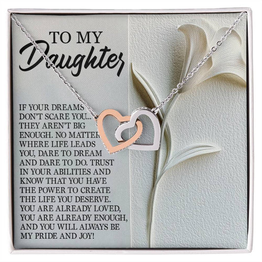 The Daughter-Dare Dream Interlocking Hearts Necklace in silver and rose gold with cubic zirconia crystals is showcased on a card with the message "To my daughter," featuring an inspirational note about dreams, courage, and love against a delicate white flower design.