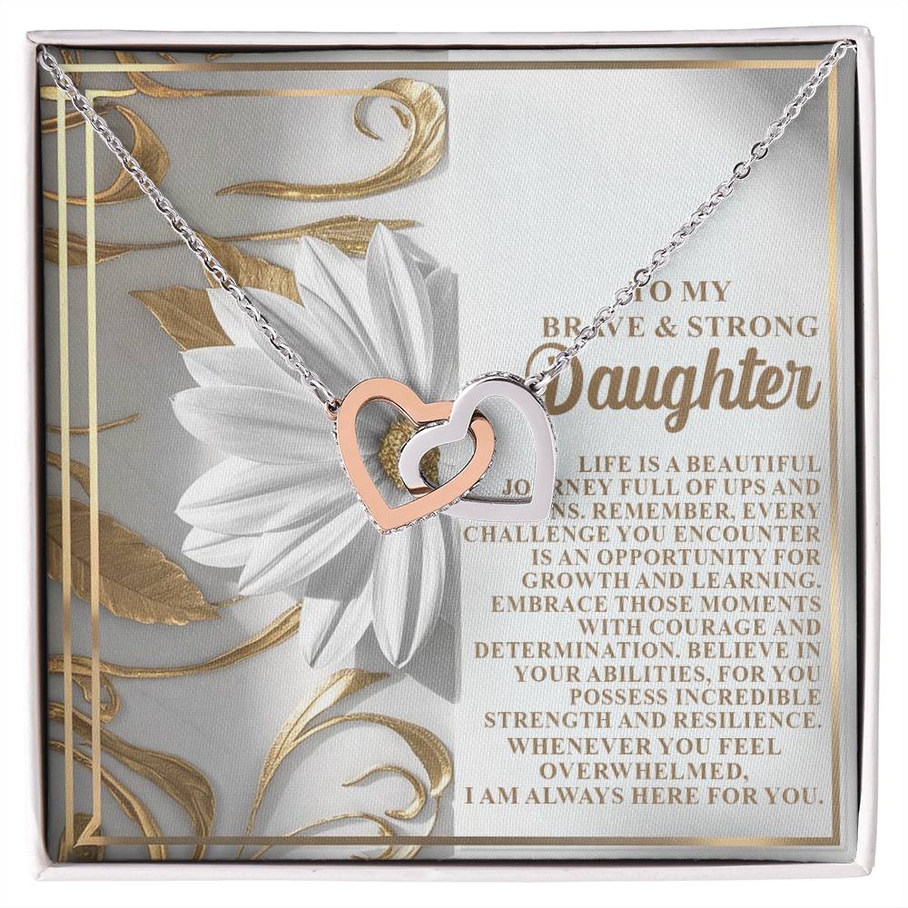 The Daughter-Here For You Interlocking Hearts Necklace, crafted with a rose gold finish and sparkling cubic zirconia crystals, is elegantly displayed against white flowers with an inspiring message celebrating a daughter's courage, growth, and resilience.
