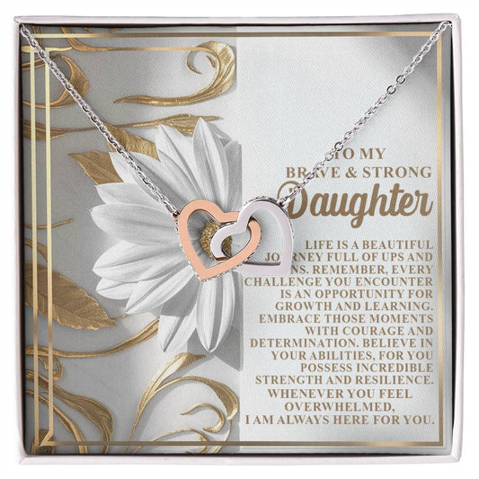 The Daughter-Here For You Interlocking Hearts Necklace, crafted with a rose gold finish and sparkling cubic zirconia crystals, is elegantly displayed against white flowers with an inspiring message celebrating a daughter's courage, growth, and resilience.