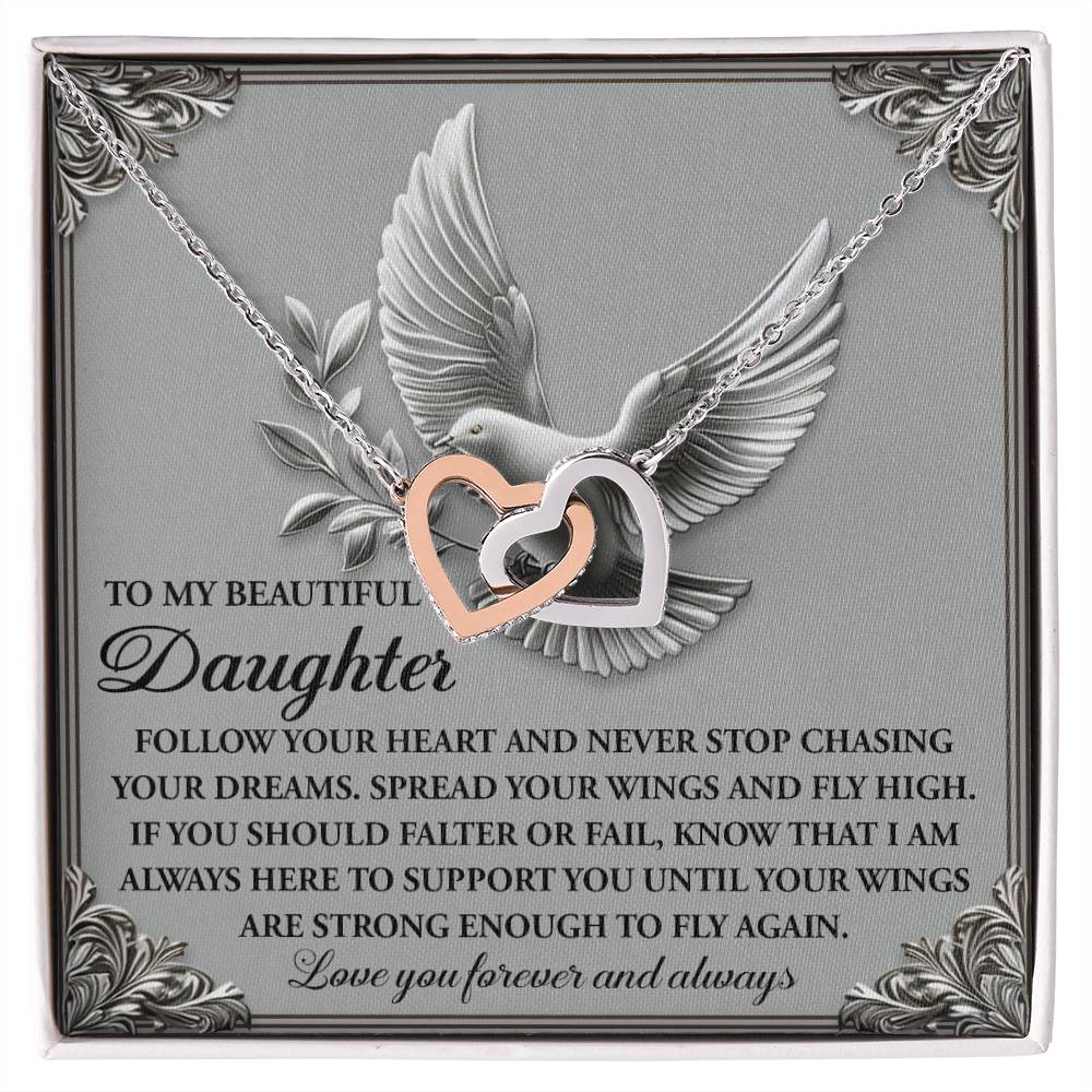 The "Daughter-Your Wings" necklace features two interlocking heart pendants in surgical steel with a rose gold finish, presented on a card embossed with a dove and a message encouraging daughters to pursue their dreams until they can soar independently.