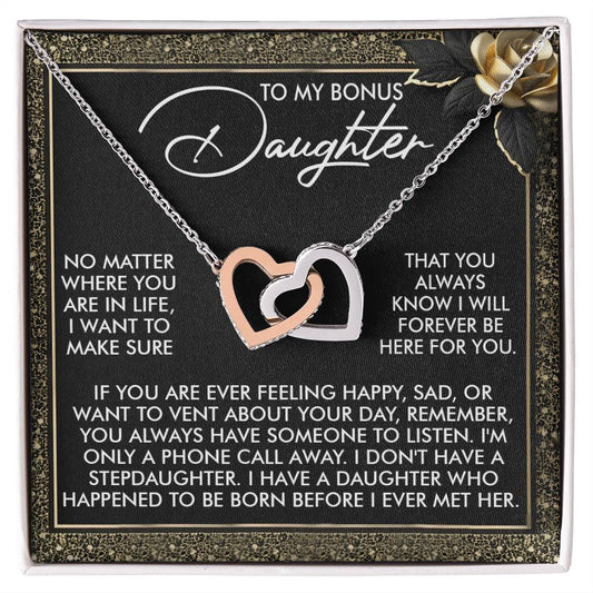The Daughter-Phone Call Interlocking Hearts Necklace, with a gold and silver heart adorned by cubic zirconia crystals, elegantly rests on a heartfelt card saying, "To my bonus daughter... No matter where you are in life... I will forever be here for you.