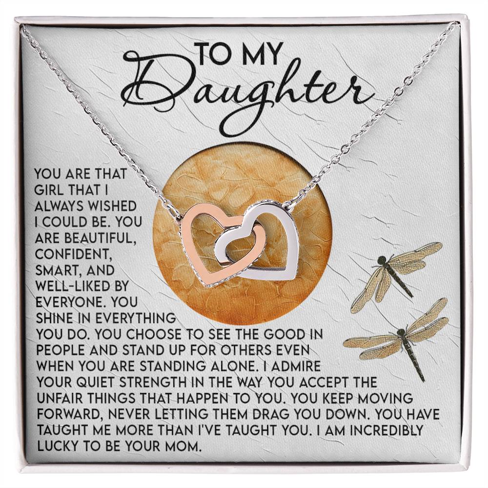 The Daughter-Quiet Strength Interlocking Hearts Necklace features a rose gold finish and is presented with a heartfelt "mother to daughter" card adorned with dragonfly illustrations, celebrating her beauty, confidence, and strength.