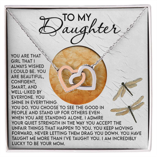 The Daughter-Quiet Strength Interlocking Hearts Necklace features a rose gold finish and is presented with a heartfelt "mother to daughter" card adorned with dragonfly illustrations, celebrating her beauty, confidence, and strength.