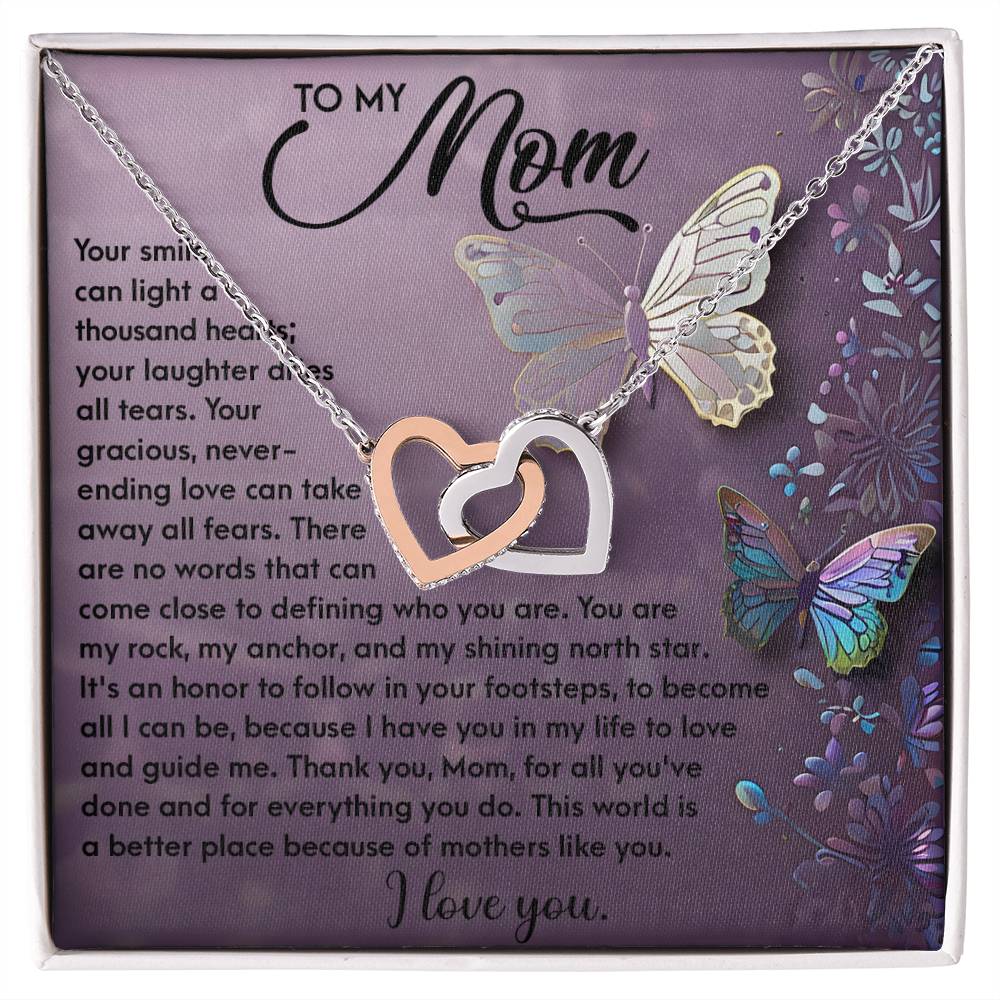 The Mom-Shining Star Interlocking Hearts Necklace in silver and rose gold, featuring cubic zirconia crystals, is displayed on a butterfly-adorned purple card with a loving message of appreciation to a mother.