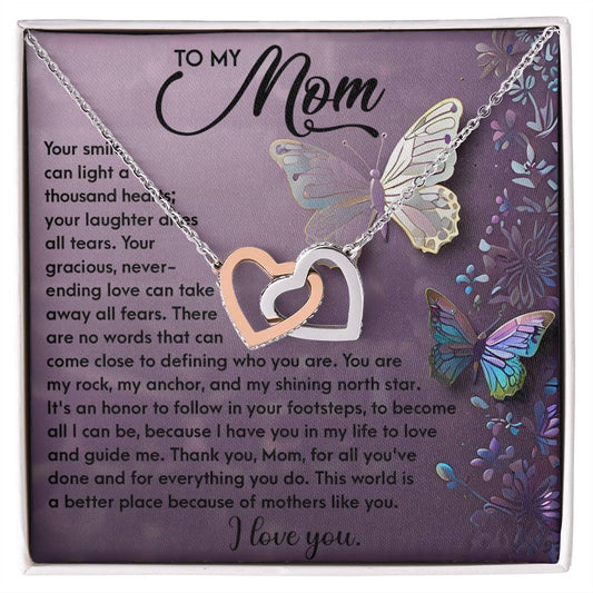 The Mom-Shining Star Interlocking Hearts Necklace in silver and rose gold, featuring cubic zirconia crystals, is displayed on a butterfly-adorned purple card with a loving message of appreciation to a mother.
