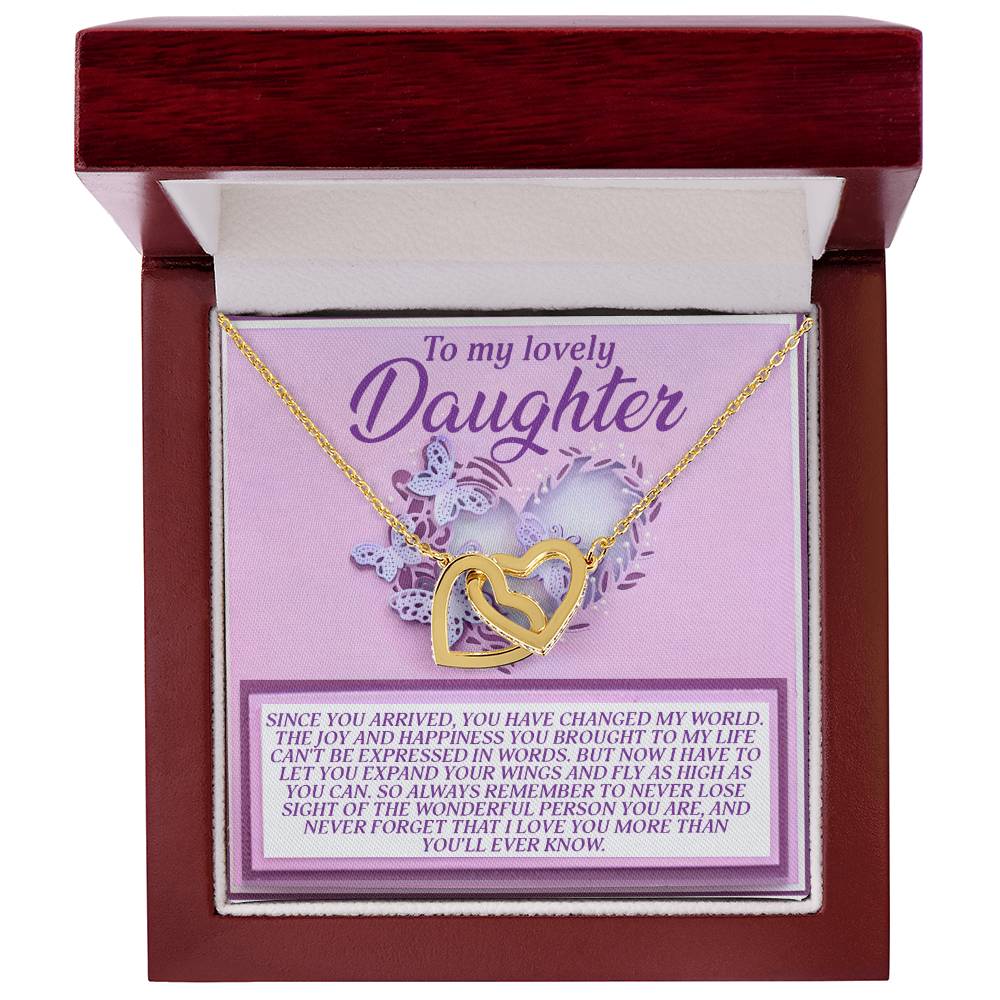 An open jewelry box showcases the Daughter-Expand Wings - Interlocking Hearts necklace, with a rose gold finish and cubic zirconia crystals. The card inside bears a heartfelt "To my lovely Daughter" message and features a purple floral design. The box is lined with white fabric.