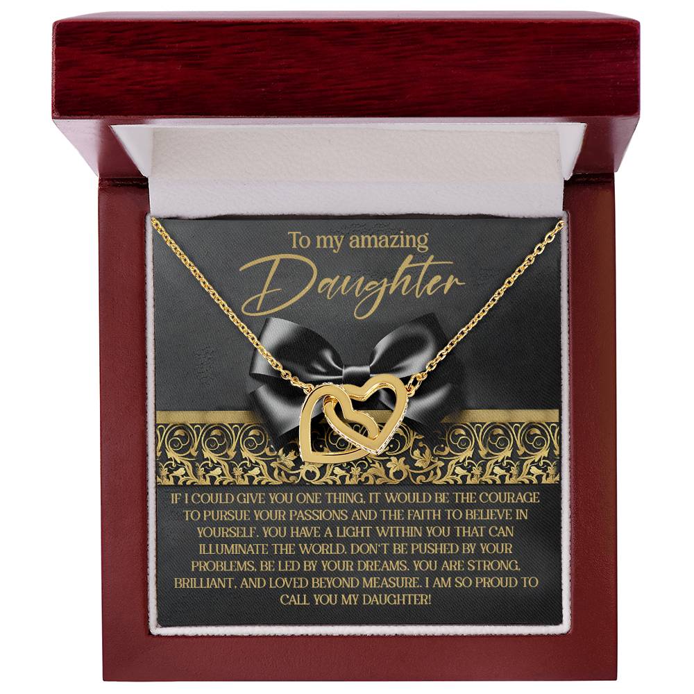 The Daughter-Pursue Passions Interlocking Hearts Necklace, a gold heart-shaped piece with cubic zirconia crystals, comes in a gift box labeled "To my amazing Daughter." It includes a card decorated with a black ribbon and floral design, featuring an inspirational message of pride and love.