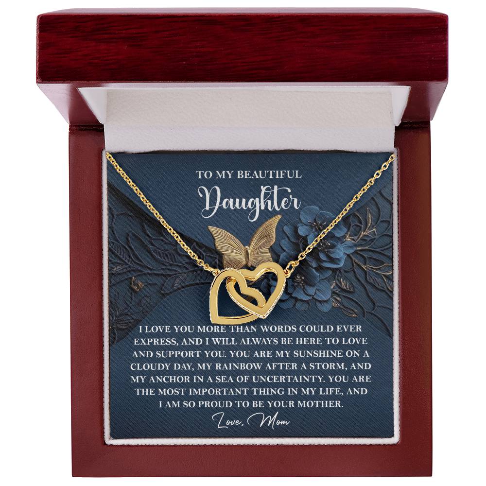 The "Daughter-In My Life - Interlocking Hearts Necklace" showcases intertwined heart and butterfly designs on a gold pendant, adorned with cubic zirconia crystals. It comes elegantly presented in a jewelry box with a heartfelt message from mother to daughter.