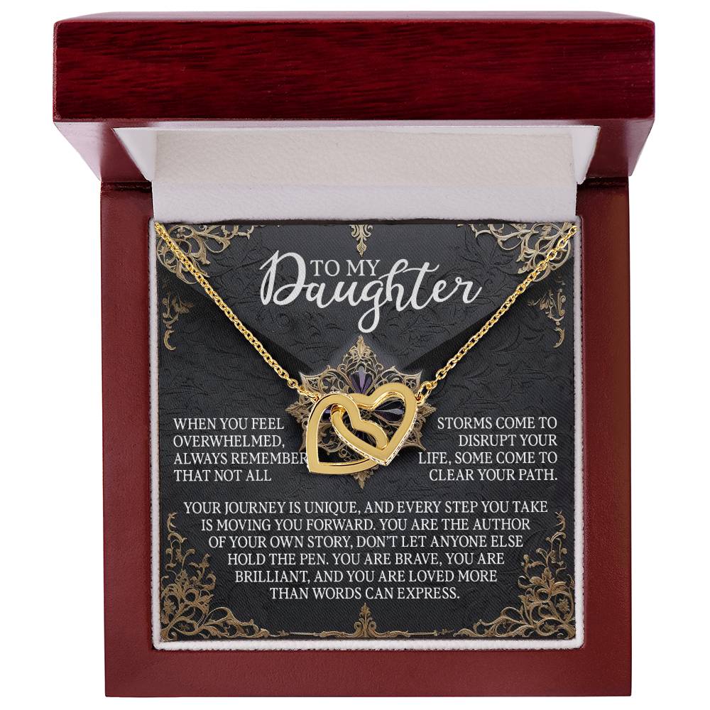 The Daughter-The Pen - Interlocking Hearts Necklace, embellished with shimmering cubic zirconia crystals, comes in a red velvet box. The lid displays "To My Daughter" with an inspiring message on a dark, ornate backdrop—an ideal gift for her.