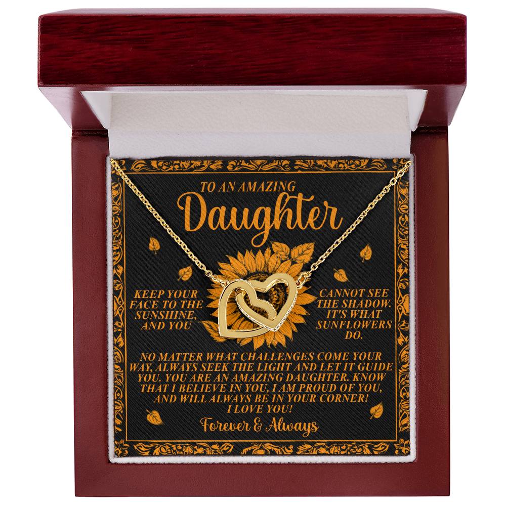 The Daughter-Seek Light Interlocking Hearts Necklace, showcasing two gold hearts with a rose gold finish, comes in a dark wooden box. It's accompanied by a card adorned with sunflower graphics and messages like, "I love you forever & always," for an "Amazing Daughter.