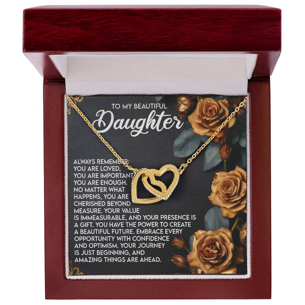 The Daughter-Loved Enough Interlocking Hearts Necklace with a rose gold finish rests in a velvet box, surrounded by golden roses. Cubic zirconia crystals shine, emphasizing a loving message of encouragement for the future.