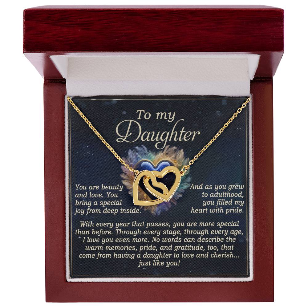 The "Daughter-Like You" Interlocking Hearts Necklace, with a rose gold finish and cubic zirconia crystals, is elegantly displayed in an open red velvet box. The lid carries a heartfelt note for a daughter, expressing love and pride against a colorful abstract background.