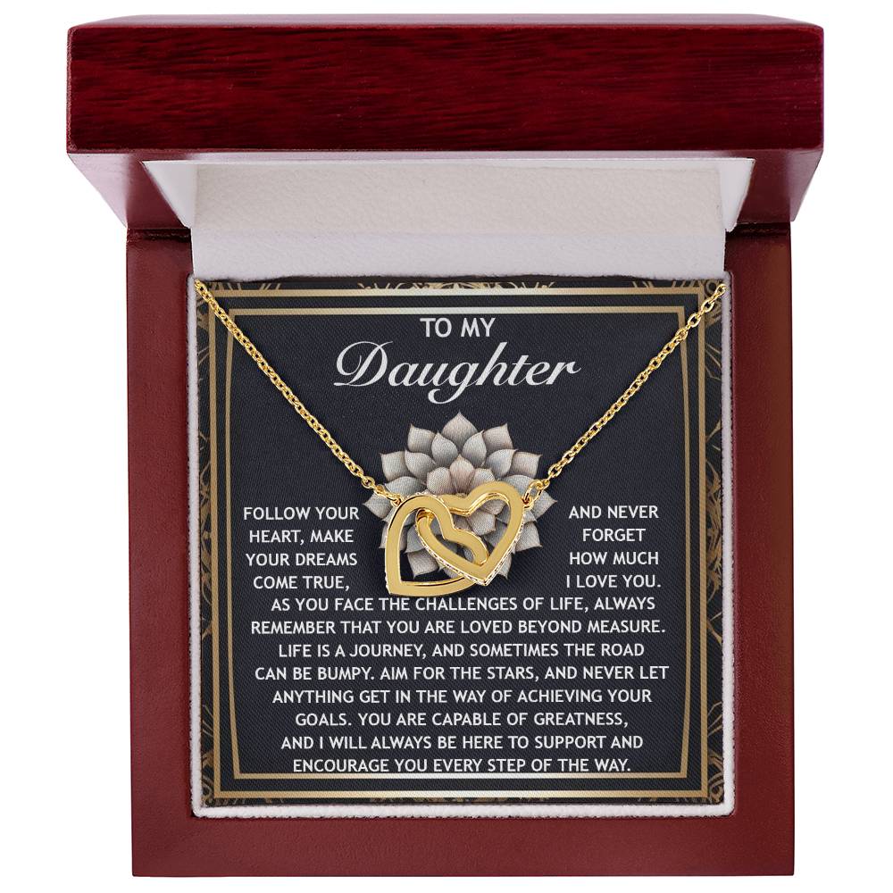 The Daughter-In The Way - Interlocking Hearts Necklace features a rose gold finish and cubic zirconia crystals. It comes in a wooden box with an inscribed message inside the lid, offering love and support to encourage your daughter in facing life's challenges.