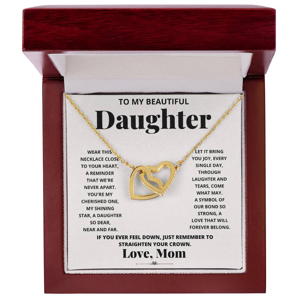 A "To My Beautiful Daughter, Wear This Necklace - Interlocking Hearts Necklace" with interlocking hearts pendants adorned with cubic zirconia crystals, presented in a box with a heartfelt message from a mother to her daughter.