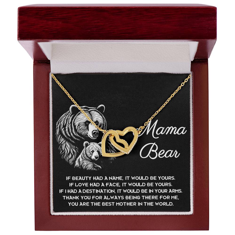 The "To Mom, In Your Arms - Interlocking Hearts Necklace" is a personalized gift with a gold heart and engraved bears saying "Mama Bear," alongside a heartfelt message about beauty, love, and gratitude. It’s presented in a wooden box with black velvet, radiant like interlocking hearts with cubic zirconia crystals.