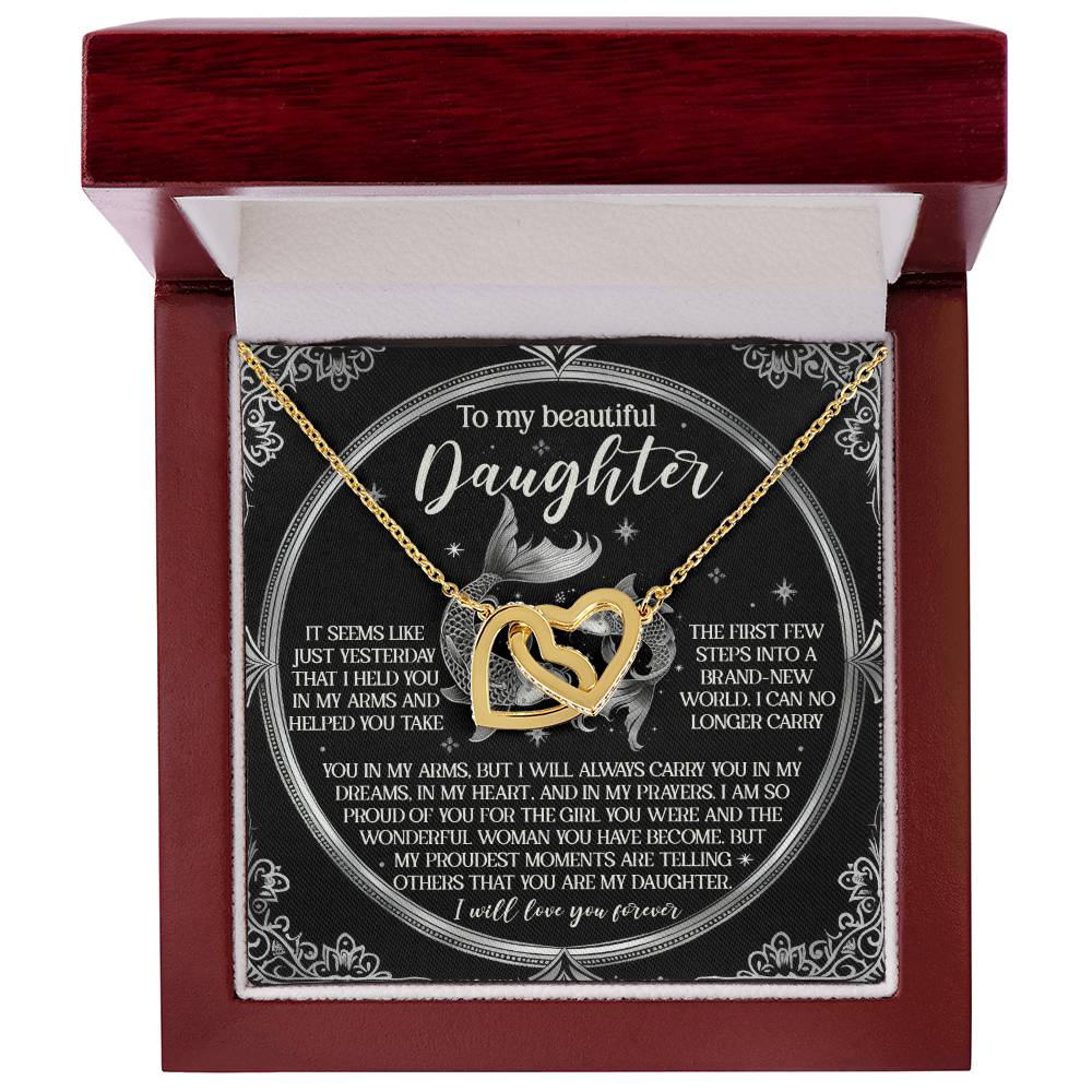 An open red box reveals the "Daughter-In My Prayers - Interlocking Hearts Necklace" adorned with gold and cubic zirconia. The lid features a heartfelt message about parental love, set against a black backdrop with delicate white floral designs.