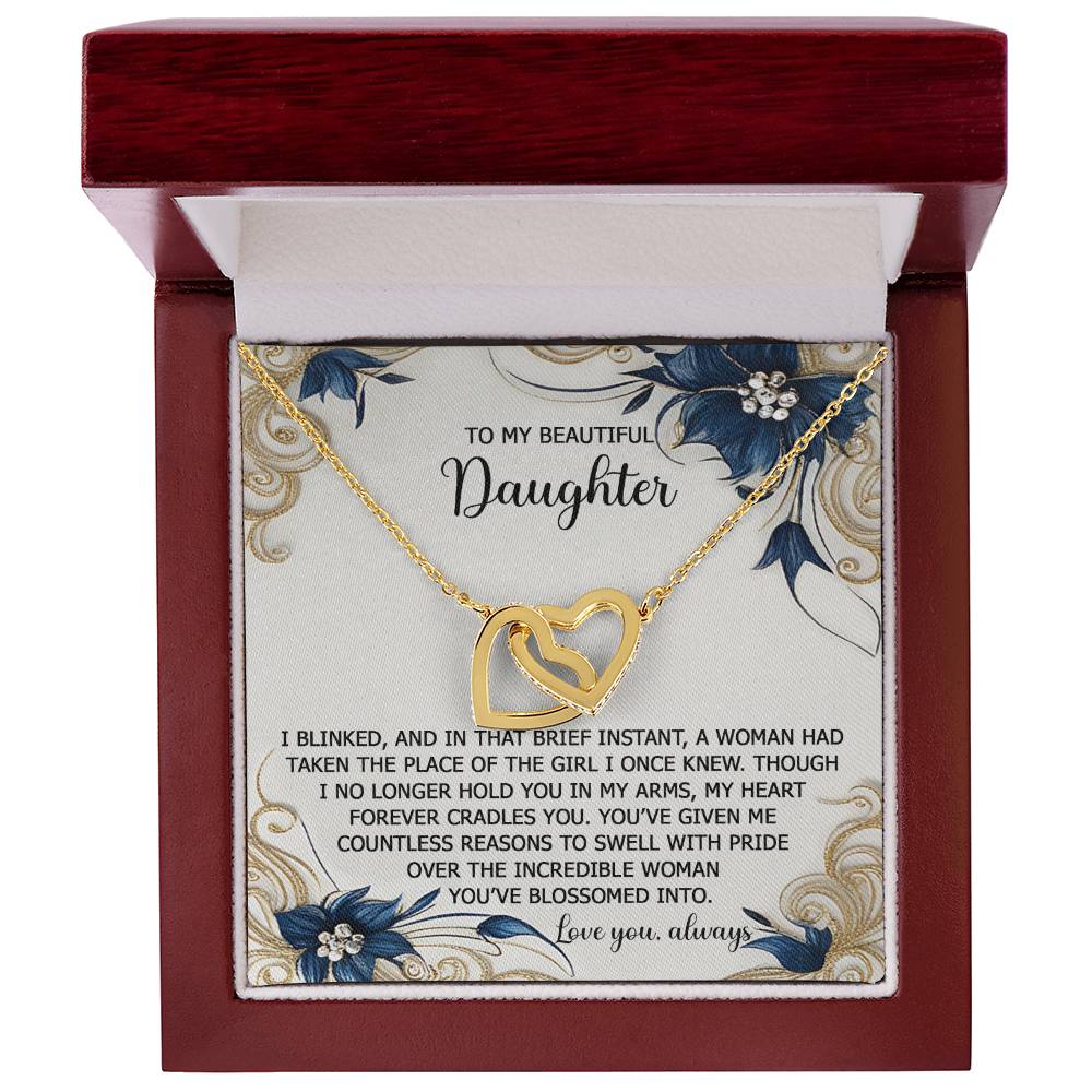 The Daughter-In My Arms - Interlocking Hearts Necklace is a gold heart piece, nestled in a wooden box, inscribed for daughters. It's adorned with cubic zirconia and floral accents, making it the perfect heartfelt gift for her.