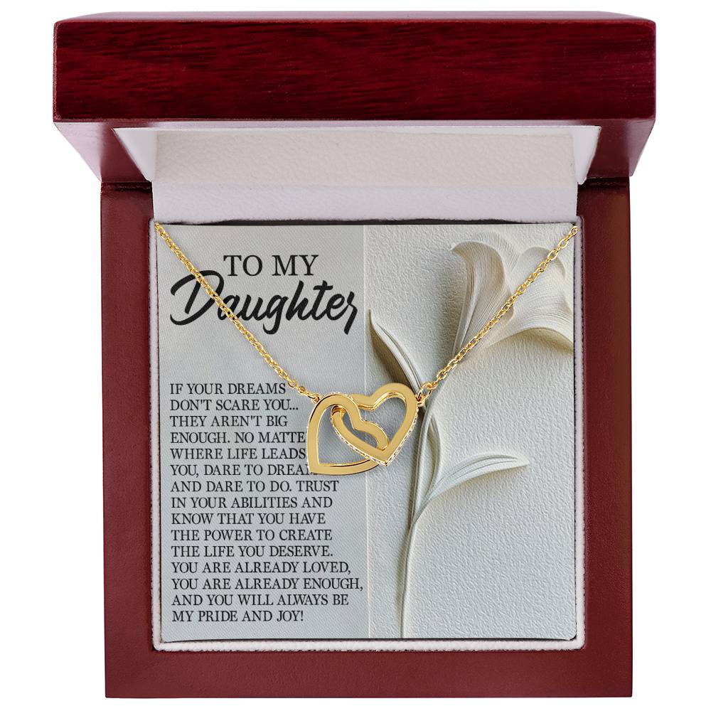 The Daughter-Dare Dream Interlocking Hearts necklace with cubic zirconia crystals is beautifully presented in a red and white gift box, accompanied by an inspirational message to a daughter, set against a floral embossed backdrop.