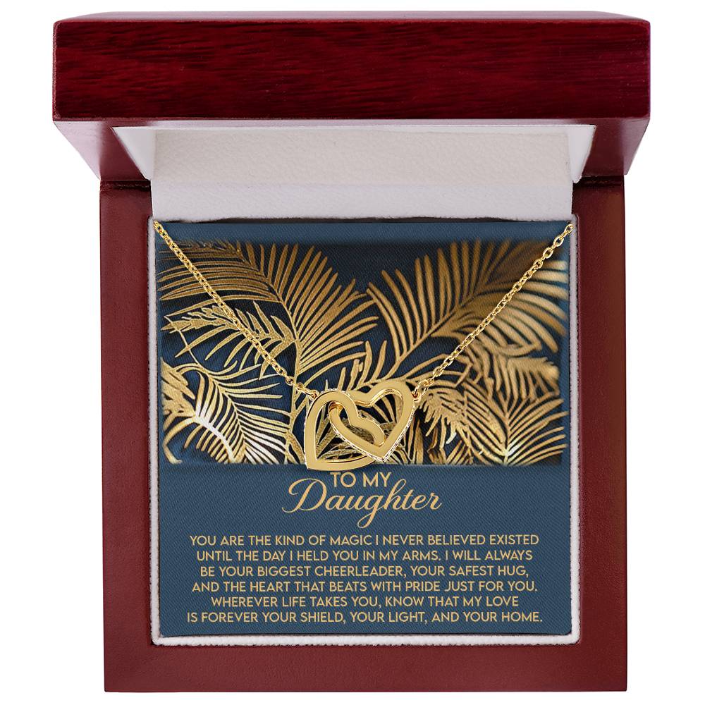 A wooden jewelry box reveals the Daughter-Your Home - Interlocking Hearts Necklace, featuring intertwined hearts with cubic zirconia and gold leaf details. An emotional "To My Daughter" message expresses love and ends with "forever your shield, your light, and your home.