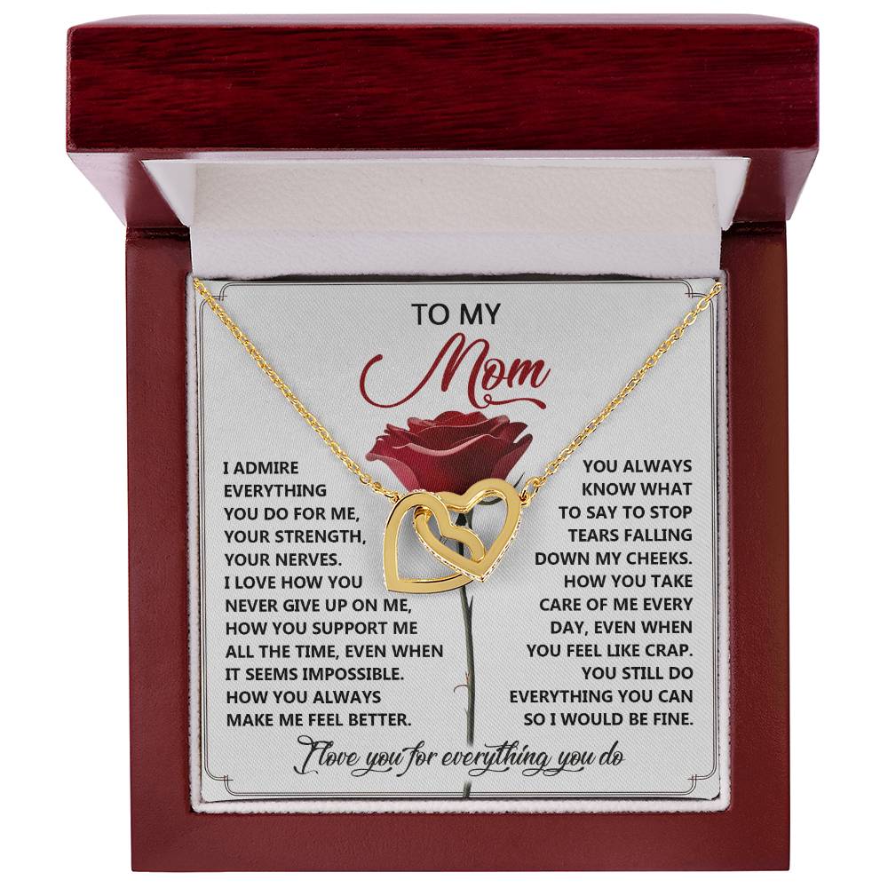 The Mom-Be Fine - Interlocking Hearts Necklace, with a rose gold finish, is elegantly presented in an open red gift box. Behind it is a heartfelt message to a mother expressing admiration, love, and gratitude for her unwavering support and care.