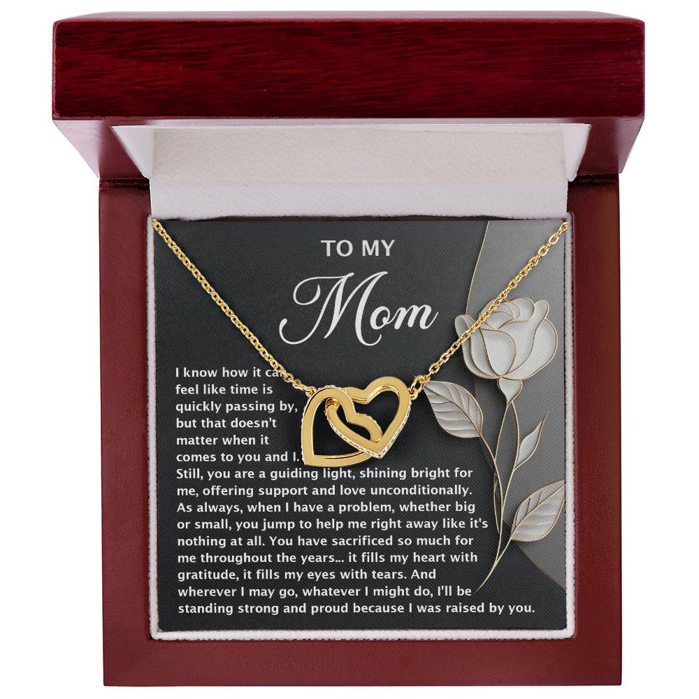 The Mom-Guiding Light - Interlocking Hearts Necklace, featuring gold intertwined heart pendants, is elegantly presented in a red gift box. The inside lid displays a touching message to "Mom" with a rose image accented by sparkling cubic zirconia crystals.